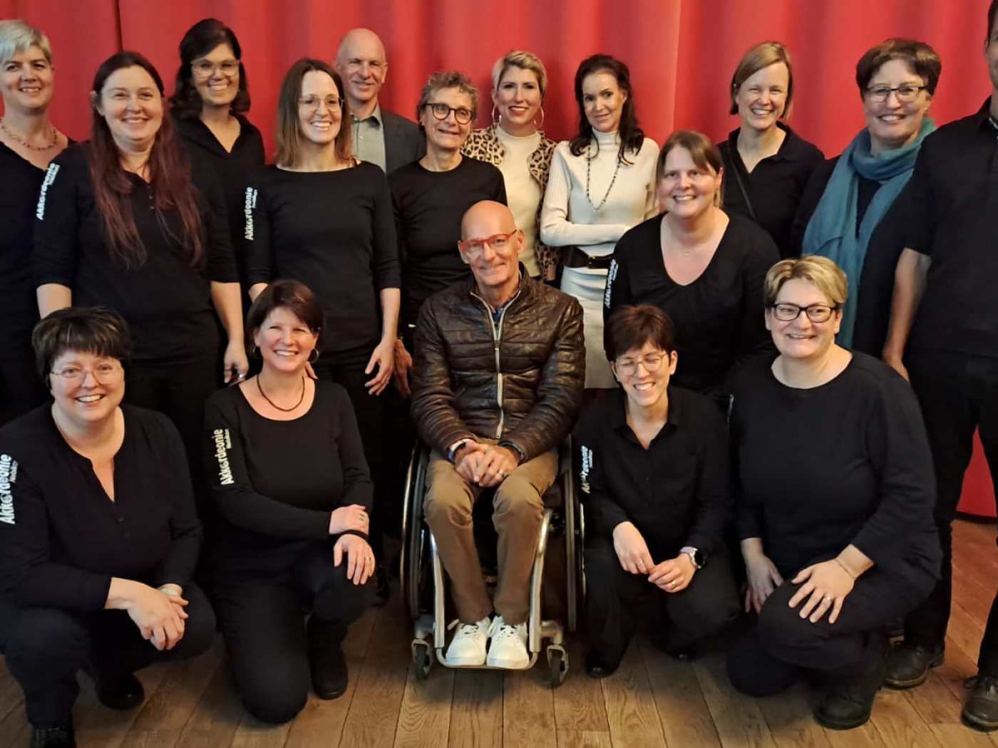 Die Akkordeonie Nebikon mit Dirigent Sven Angelo Mindeci und Gästen vor einem roten Bühnenvorhang.